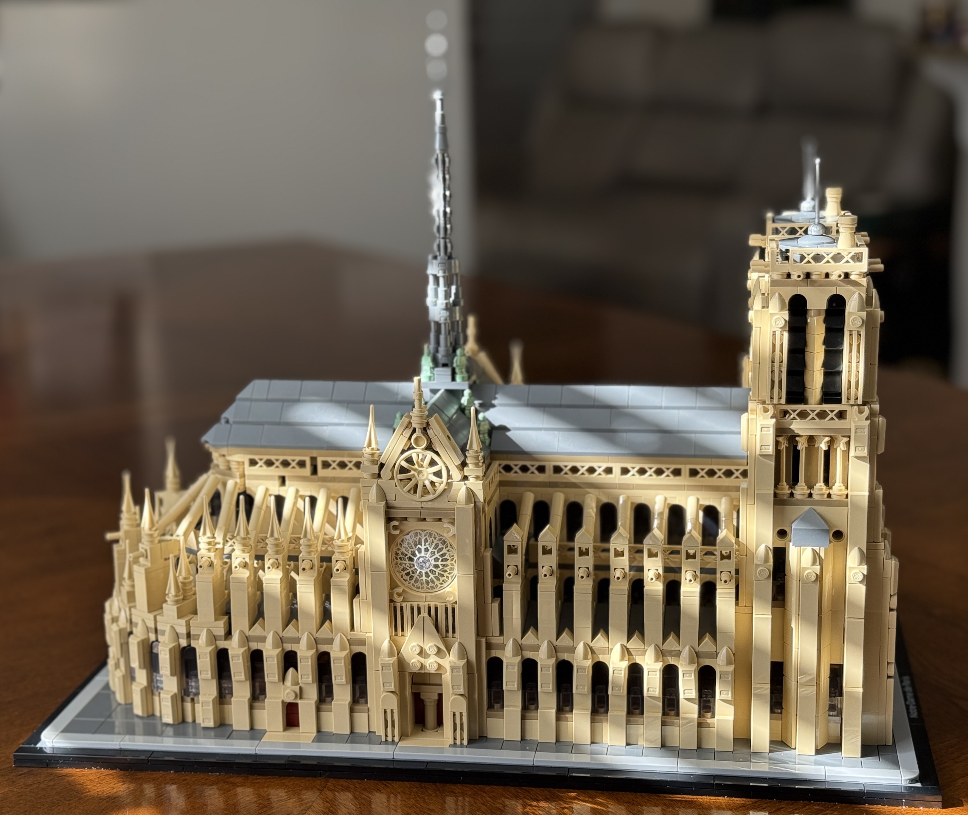 A detailed LEGO<sup>®</sup> model of the Notre-Dame Cathedral in Paris, France, showcasing its intricate Gothic architecture, including the rose window, spire, and twin towers, placed on a wooden table in a softly lit room.