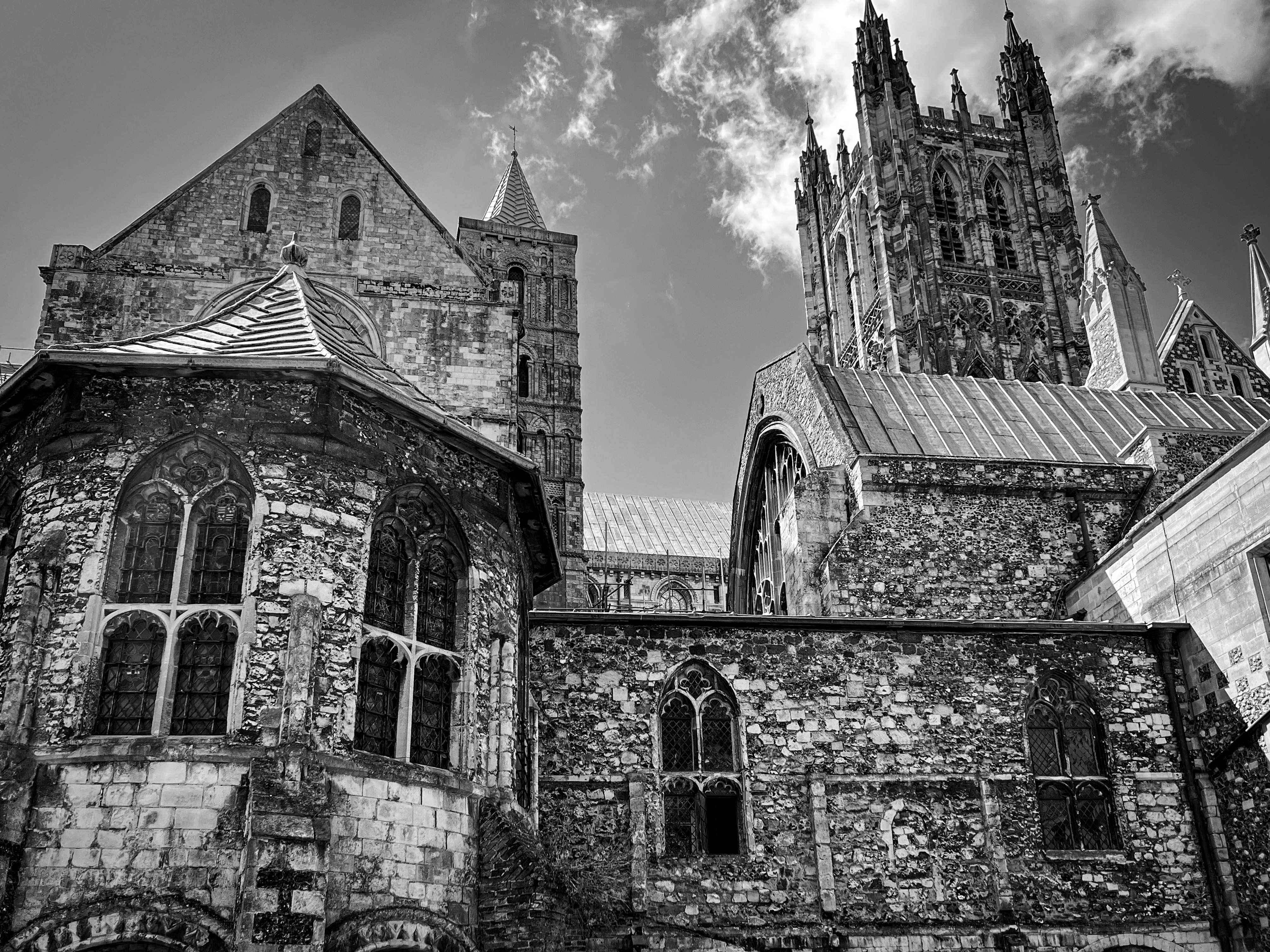 A black and white photo of a medieval cistern at Canterbury Cathedral in Canterbury, Kent, England. The cistern itself is a cylindrical add-on to the main part of the building and appears on the left side of the image. Rising in the background is the cathedral's bell tower.