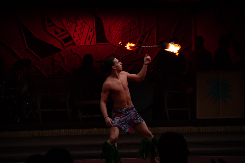 A performer tosses flame sticks in front of a red background at Walt Disney World’s Ploynesian Village Resort