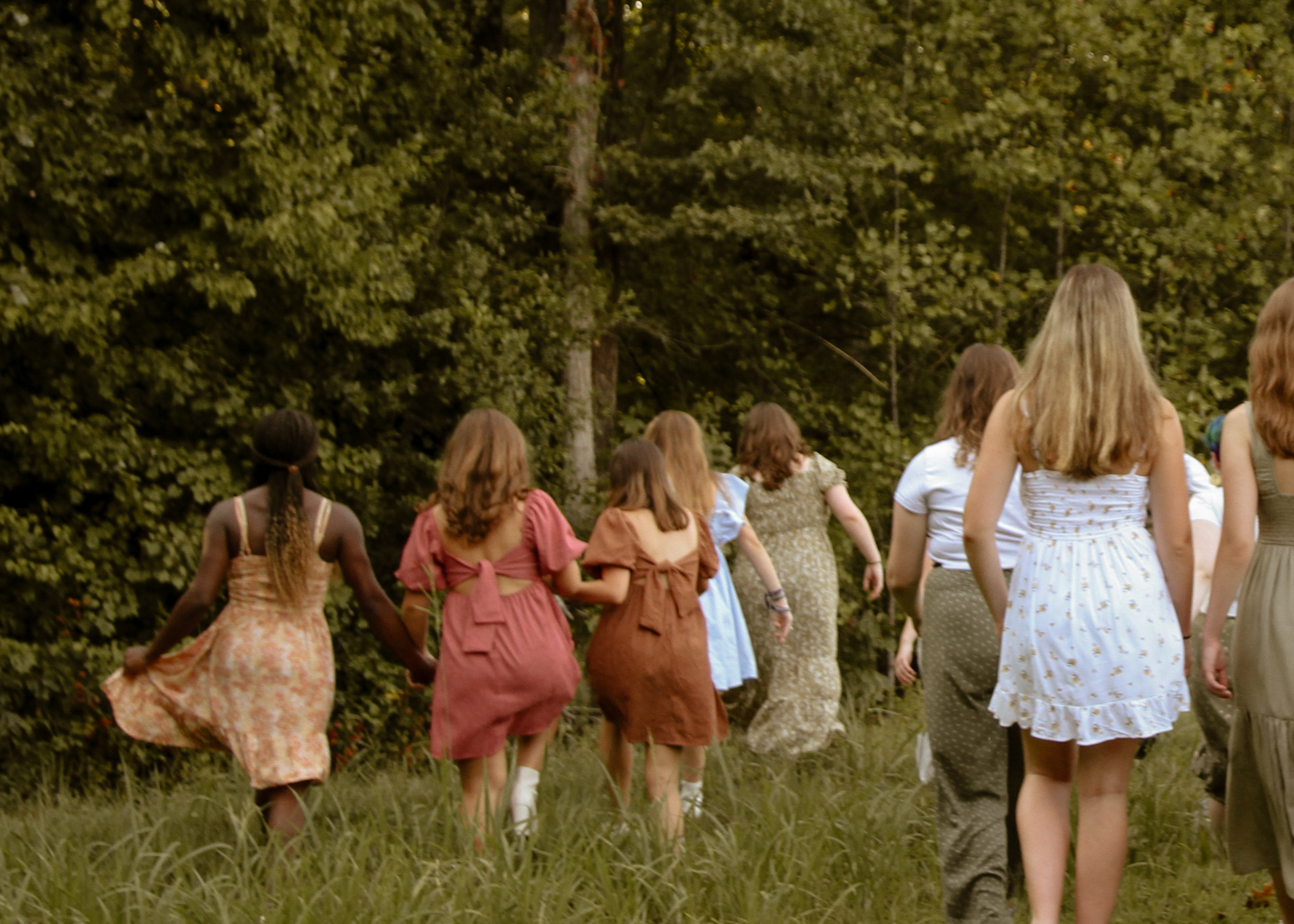 Females walking toward a tree line in tall grass away from the camera